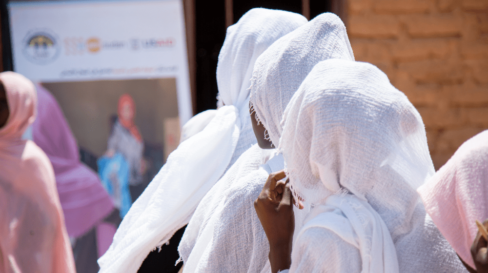 Mujeres con pañuelos blancos en la cabeza miran hacia un gran cartel con una mujer y un logotipo del UNFPA
